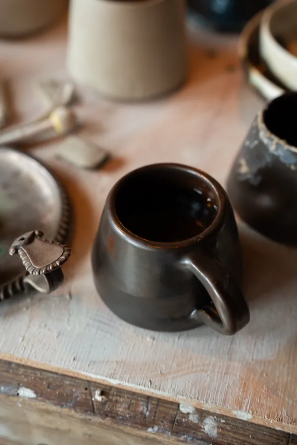 A dark glazed mug on the pottery workbench